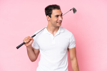 Young golfer player man isolated on pink background looking to the side and smiling