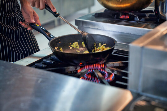Chef is stiring fire vegetable on hot pan with realistic fire frame in kitchen.