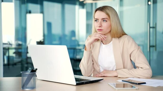 Young businesswoman showing raised index finger up gesture in moment of inspiration of new idea while working on laptop while sitting in modern office. Employee found the answer to solve the problem