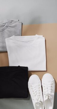 Vertical video of multi coloured t shirts and white sneakers with copy space on grey background
