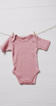 Vertical video of pink baby grow hanging on clothes pegs with copy space on white background
