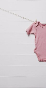 Vertical video of pink baby grow hanging on clothes pegs with copy space on white background