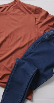 Vertical video of orange t shirt, denim trousers, shoes and copy space on white background