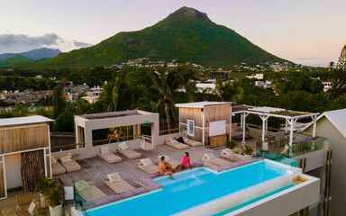 Man and Woman watching sunrise by a swimming pool, a couple on a honeymoon vacation in Mauritius with on the background the Tamarin mountain