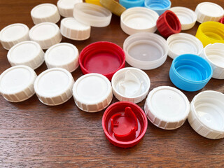 Round plastic caps of different colors and sizes lie in one pile on a brown wooden surface, close-up, top view. Garbage sorting. Recycling. Caring for the environment.