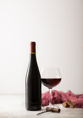 Glass and bottle of red wine with red towel and corkscrew on light background.