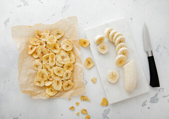 Fresh banana and baked crunchy chips snack on light kitchen background with knife.