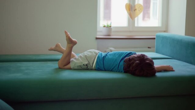 Bored child lying on couch with nothing to do, restless little boy grounded at home struggles with boredom