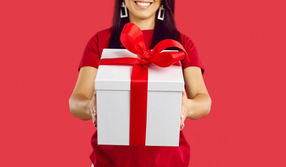 Close up of woman isolated on red studio background stretch beautiful wrapped present with bow. Female make surprise give gift box congratulate with special occasion. Bonus concept.