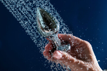 Woman washing silver anal plug under shower on blue background. 