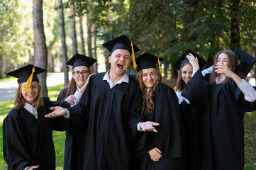 A group of graduates in robes congratulate each other on their graduation outdoors.