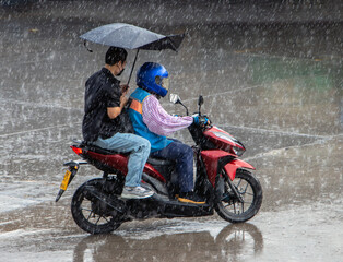 A motorcycle taxi driver with passenger rides in a heavy rain, Thailand