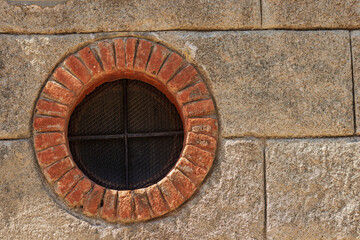 Close-up of a small round window with brick frame and iron security bars. Small village of Framura, La Spezia province, Liguria, Italy, Europe.