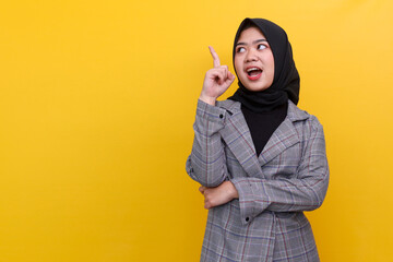 Young cheerful Asian muslim woman pointing aside to the copy space on the left standing over yellow background. 