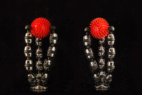 Two red hard tactile massage balls  with spikes is clamped between the flexible legs of a GorillaPod tripods  on a black background.