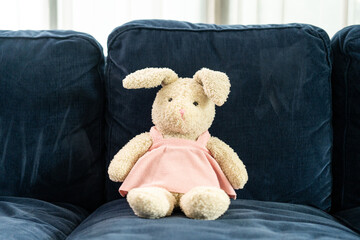 Soft fluffy rabbit doll with long ears put on sofa. Easter Bunny on a blue couch in the house. Kid...