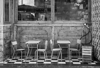 Metal vintage tables and chairs stand at the window of an old cafe on a black and white tile.Black and white photo