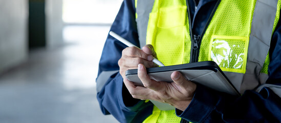 Building inspector man using digital tablet checking safety and security system in the building. Asian male worker in reflective vest working for building maintenance inspection