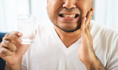 Asian man puts his hand on mouth and feels toothache because of tooth decay sensitive teeth after drinking water. Problems with teeth bad breath.