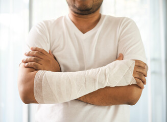 Social security and health insurance concept. Young Man suffer pain from accident fracture broken bone injury with arms splints in cast sling support arm in living room.