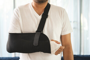 Social security and health insurance concept. Young Man suffer pain from accident fracture broken bone injury with arms splints in cast sling support arm in living room.