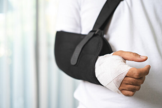 Social security and health insurance concept. Young Man suffer pain from accident fracture broken bone injury with arms splints in cast sling support arm in living room.