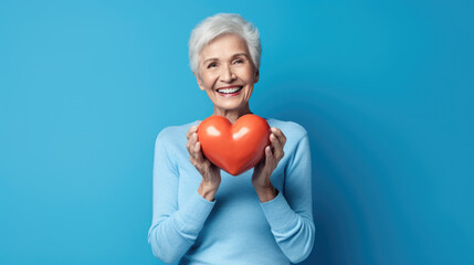 Middle-aged woman in a blue sweater hold a red heart on a blue background. Created with Generative AI technology.