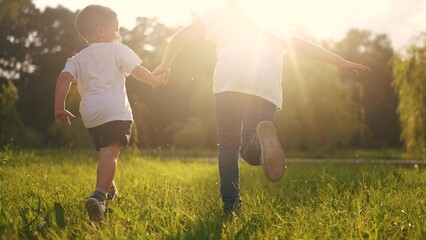 children run in the park. a boy and a girl holding hands run through the grass in the summer at sunset in the park. happy family kid dream concept. children run at sunset in summer hold hands sun © maxximmm