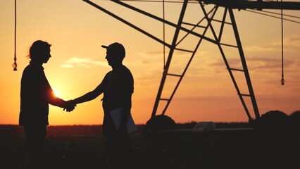Fototapeta na wymiar handshake agriculture. silhouette two farmers sign a contract shake hands on the background of an irrigation machine in a cornfield. business handshake agriculture irrigation lifestyle concept