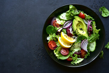 Fresh vegetable salad with avocado, cucumber, tomatoes and green leaves. Top view with copy space.