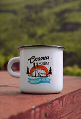 A white mug of hot tea with a mountain print stands on a wooden table. Camping lifestyle. Text - Say yes to new adventures