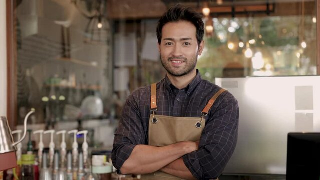 4k, portrait smiling barista attractive Indian man arms crossed standing at counter with apron, small business cafe coffee shop owner happy start up with cheerful, mature shopkeeper looking at camera