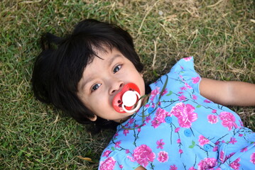 Cute little girl with pacifier lying on the grass at public park