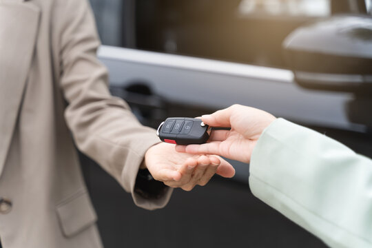 transportation rental automotive business concept. Close up hands of rental auto agent giving car remote key to client to travel sightseeing.