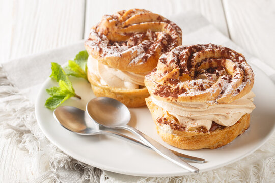 Delicious beautiful Paris Brest choux pastry cake with hazelnut cream decorated with powdered sugar and cocoa close-up in a plate on the table. Horizontal