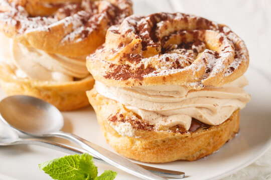 Classic French cake Paris Brest from choux pastry with cream decorated with powdered sugar and cocoa close-up in a plate on the table. Horizontal