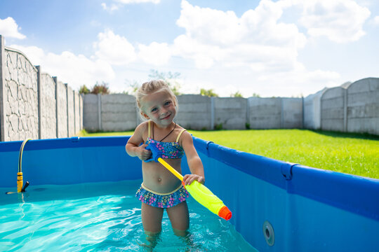 Young girl in a swimming pool aiming a water pistol and shooting. Childhood fun.