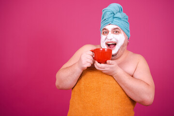 Early morning. Funny fat man enjoys life. The guy wrapped in a towel after a shower poses on a pink...