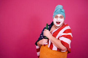 Early morning. Funny hungry fat man drinking beer. The guy wrapped in a towel after a shower poses on a pink background.
