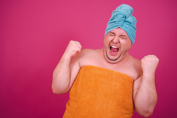 Early morning. Funny fat man enjoys life. The guy wrapped in a towel after a shower poses on a pink...