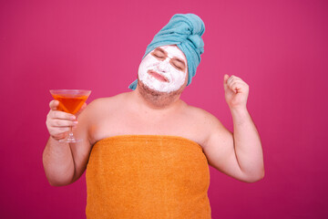 Early morning. Funny fat man drinks a cocktail before a party. The guy wrapped in a towel after a...