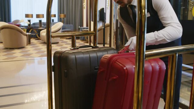 Cropped shot of bellboy putting clients luggage in special cart and delivering it to rooms in hotel
