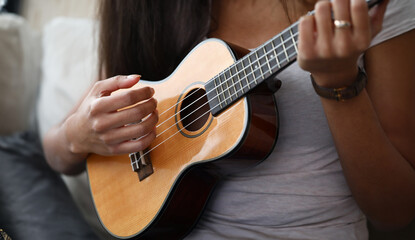 Fototapeta na wymiar Close-up of latino female hands playing on brown ukulele. African-american woman learning new melody at home. Music talent, art and entertainment concept