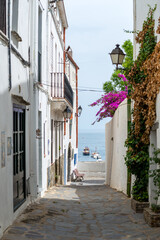 Cadaqués, view from a narrow street with traditional white houses to the port with boats - June...