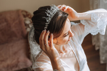 a beautiful bride in a white robe with an open bust and a crown on her head. The bride is preparing for the wedding. bride's fees the wedding day of the newlyweds. © Vasil