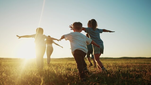 Kids Run In The Park At Sunset. Friendly Family Children Camp Kid Dream Concept. A Group Of Children Run On The Grass At The Rays Fun Of The Sun Silhouette. Childhood Dream Teamwork Sunset Concept