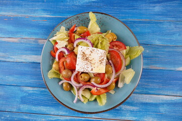 Greek salad with feta cheese and green olives on blue background