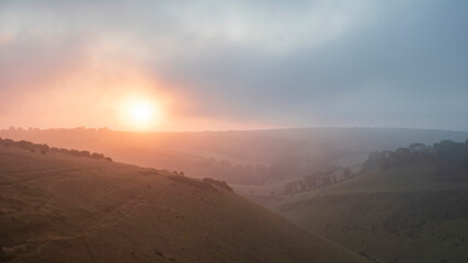Stunning Summer sunrise from Devil's Dyke in South Downs National Park in English countryside with low lying clouds giving moody feeling
