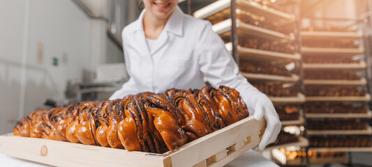 Happy worker woman baker in chef uniform hold freshly bakery poppy seed bun bread. industrial...