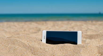 cell phone buried in the sand of a majestic summer day beach